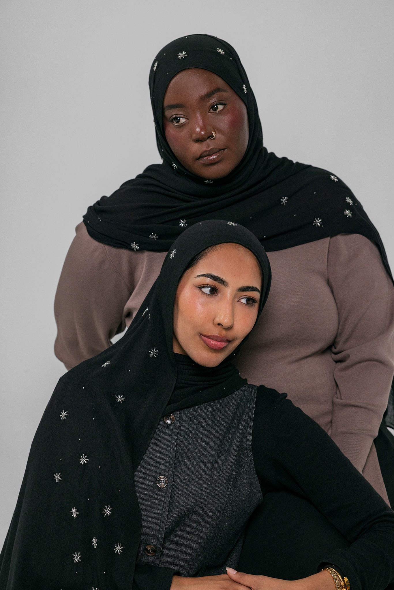 Two women wearing black hijabs with star patterns on a gray background