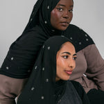 Two women wearing black headscarves with star patterns against a gray background