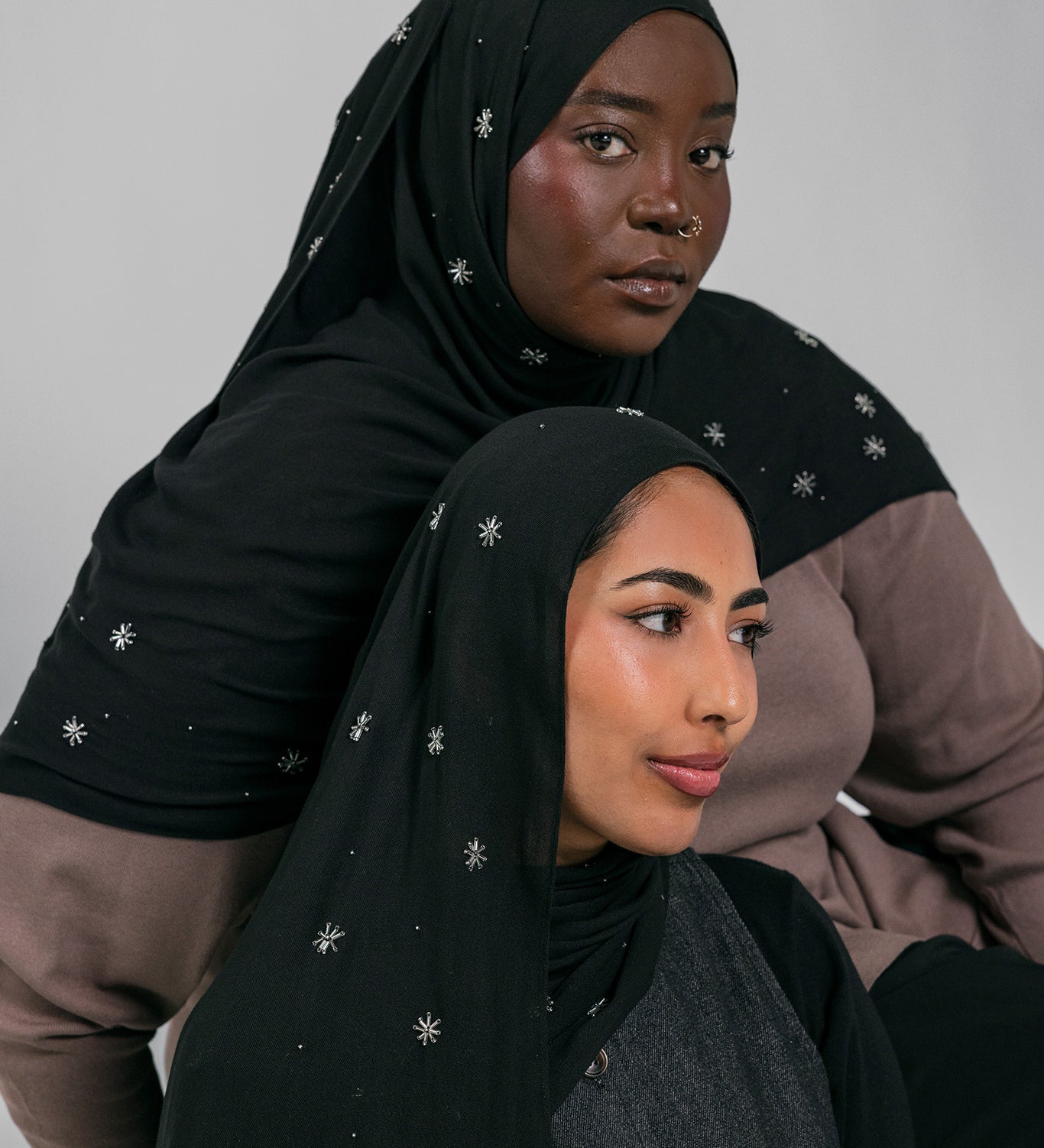Two women wearing black headscarves with star patterns against a gray background
