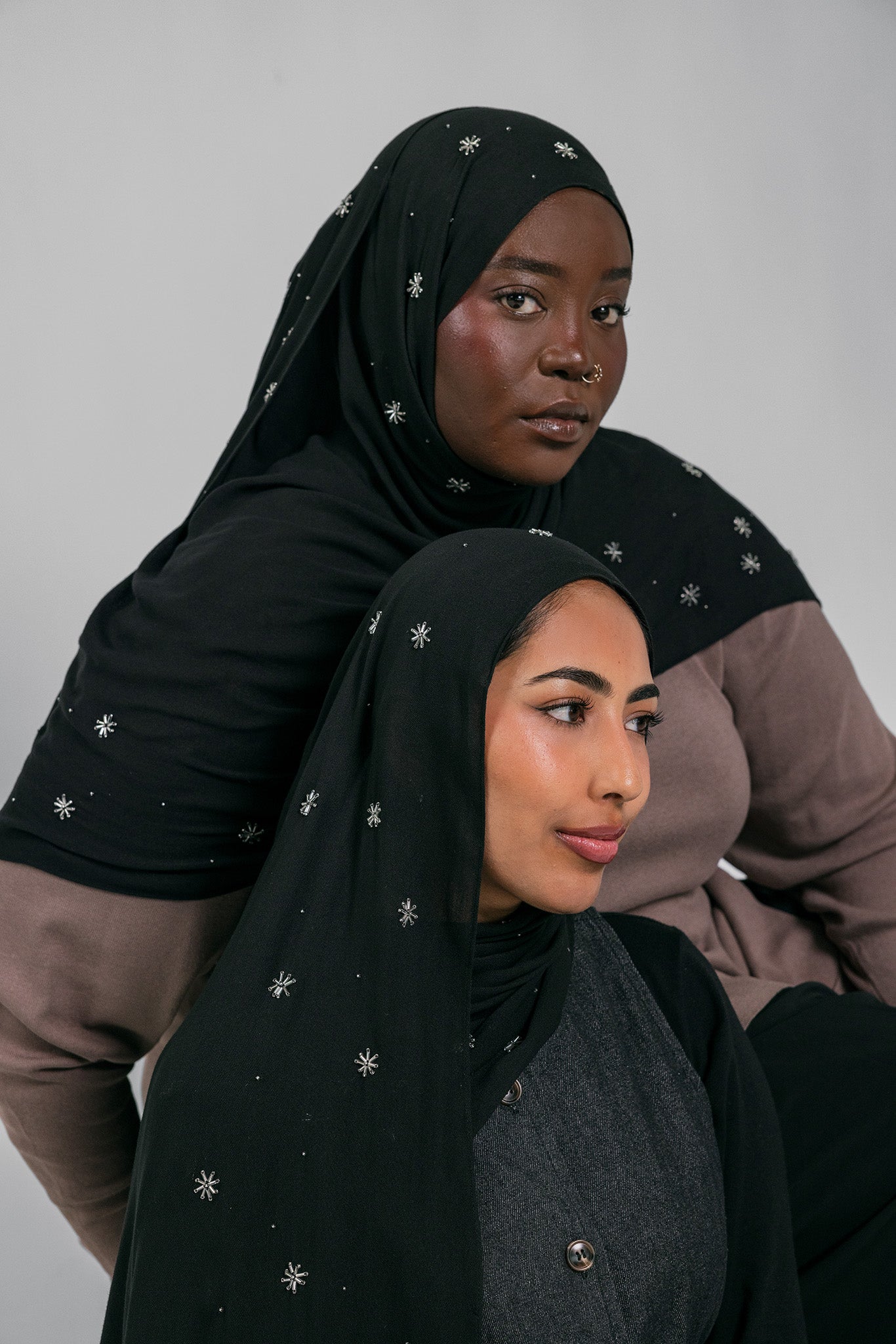 Two women wearing black headscarves with star patterns against a gray background