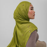Woman wearing a green hijab with gold embellishments on a plain background