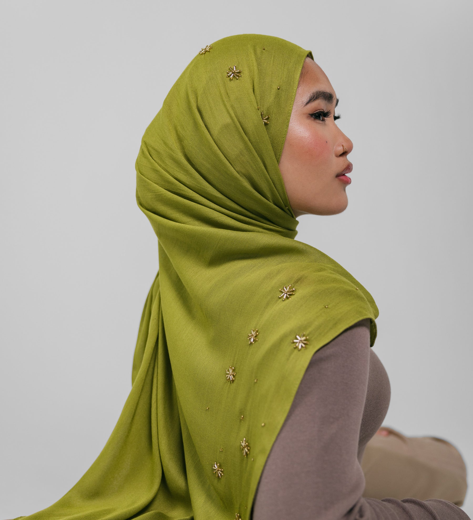 Woman wearing a green hijab with gold embellishments on a plain background