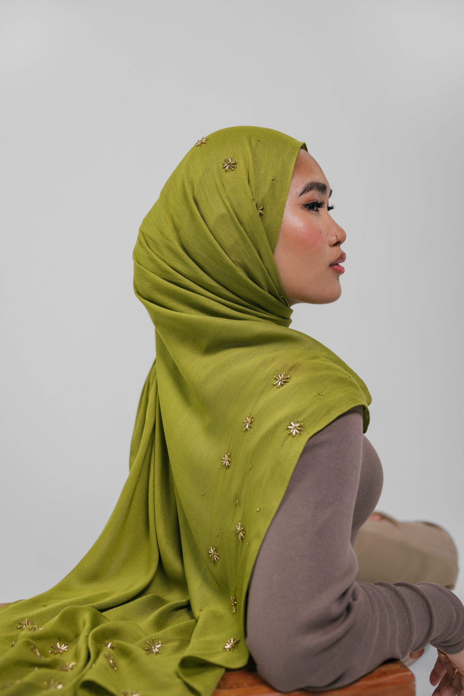 Woman wearing a green hijab with gold embellishments on a plain background