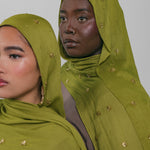 Two women wearing green headscarves with gold embellishments against a plain background