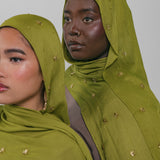 Two women wearing green headscarves with gold embellishments against a plain background