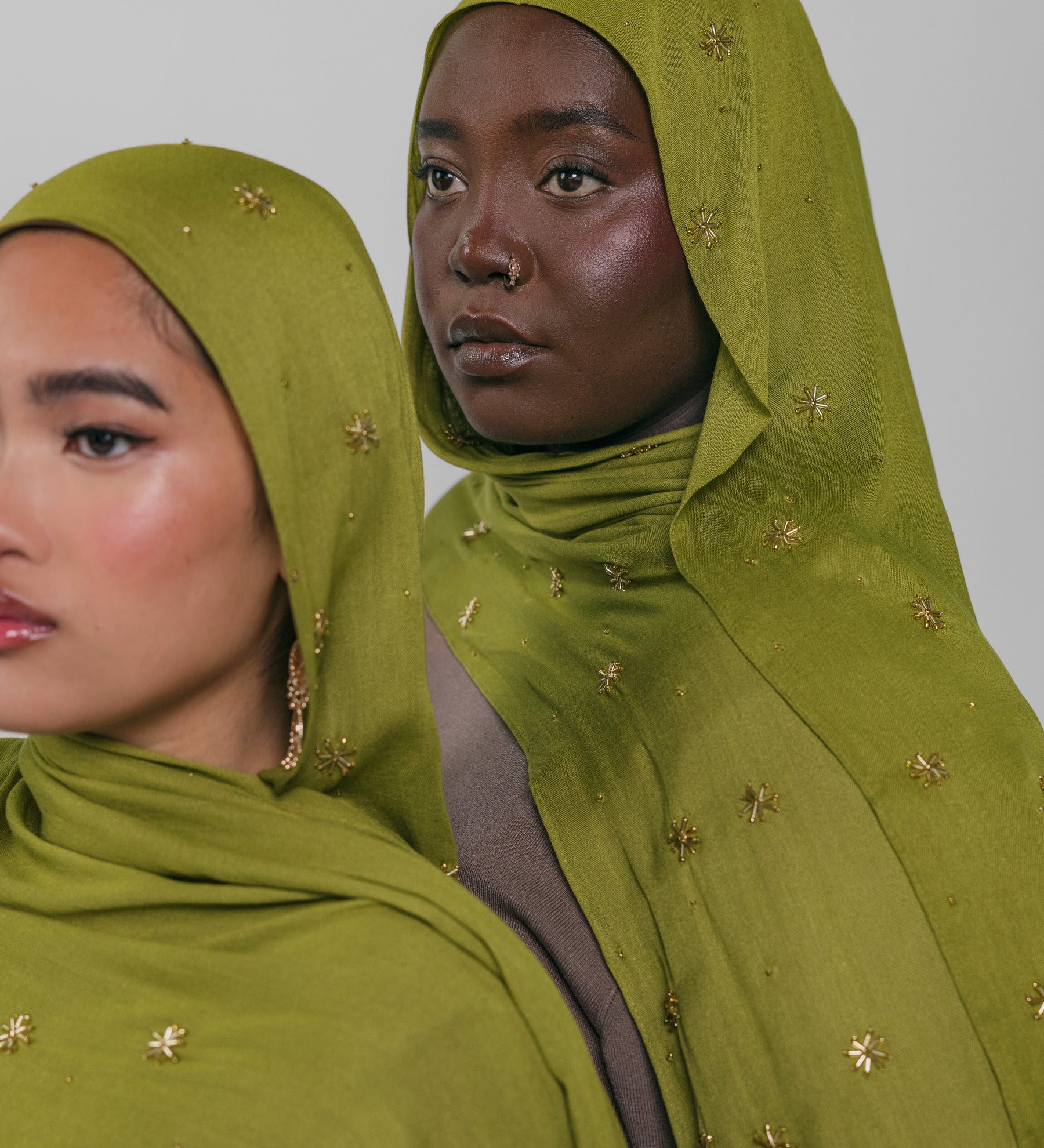 Two women wearing green headscarves with gold embellishments against a plain background