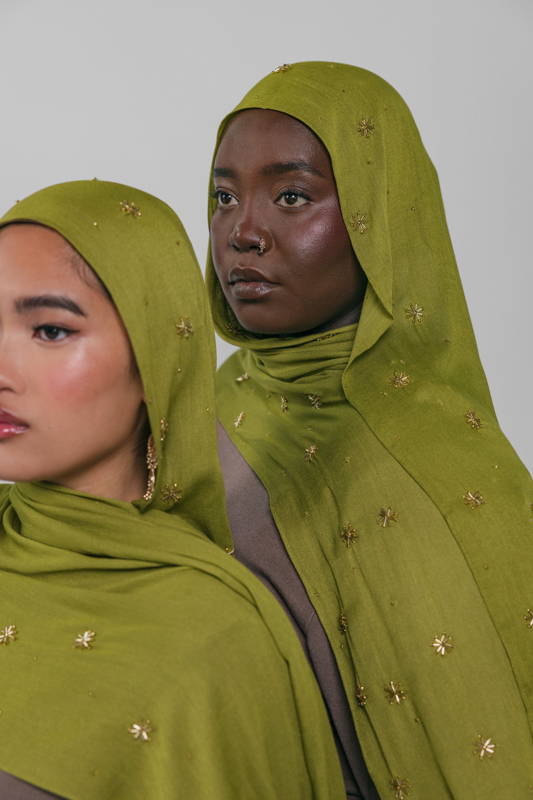Two women wearing green headscarves with gold embellishments against a plain background