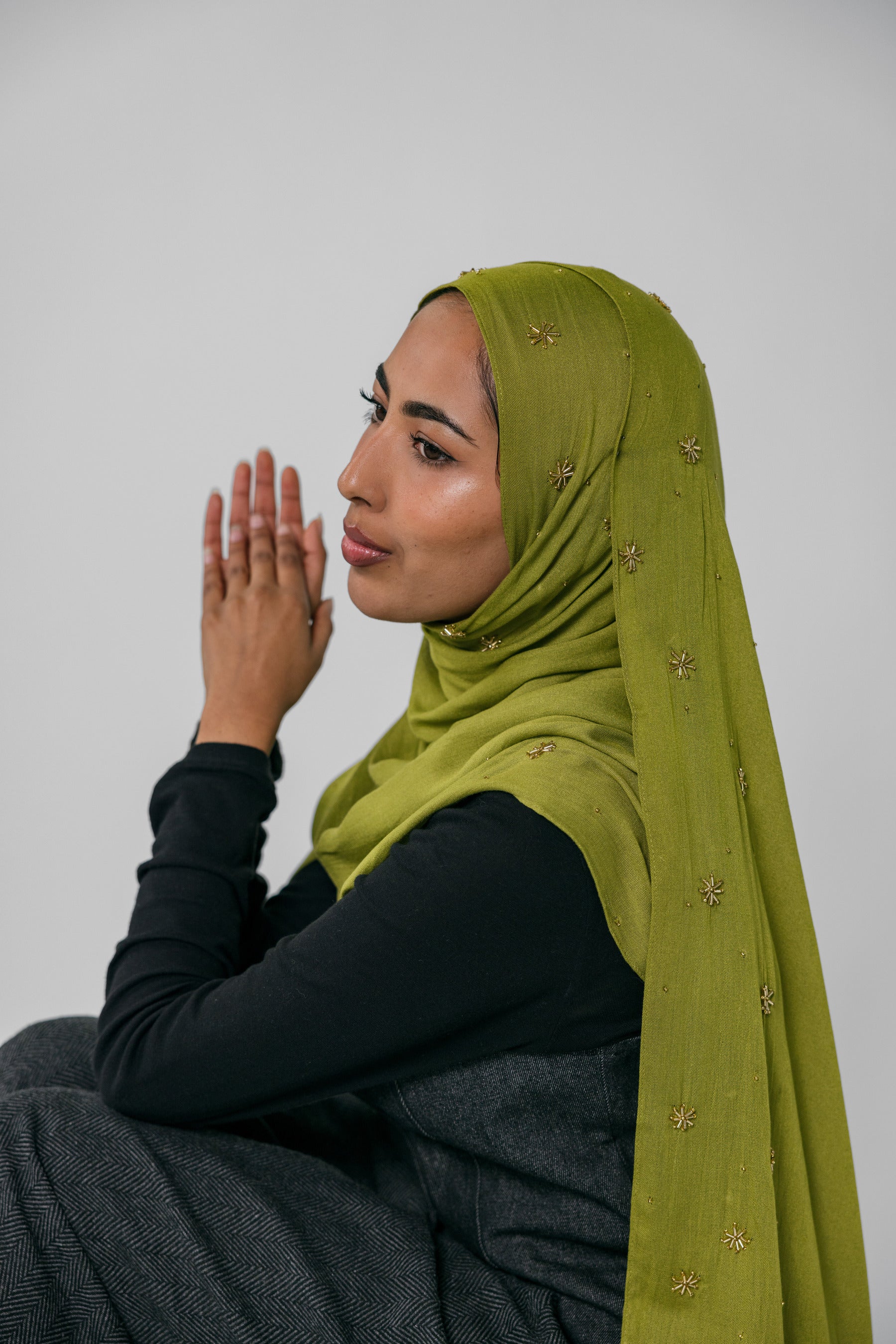 Woman wearing a green hijab with gold embellishments against a plain background