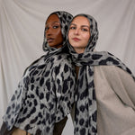 Two women wearing black and white leopard print scarves against a plain background