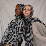 Two women wearing black and white leopard print scarves against a plain background