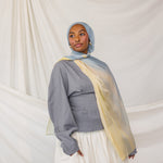 Model wearing a gray top, white skirt, and blue to yellow gradient hijab against a plain background