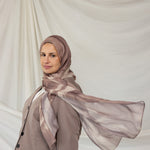 Woman wearing a brown gray sediment printed hijab and coat against a plain background
