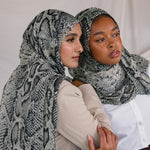 Two models posing together showing their Ink Cobra VELA hijab. This hijab features greys, blacks, and whites in a snakeskin-like pattern. 