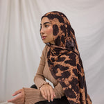 Model shown wearing Wild Savanna, a scarf from VELA that features a peach/orange/tan base that mimics and animal print, and dark brown spots. 