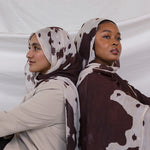 Two models shown posing back to back, both wearing the Prairie Hide print that is a cow/western inspired print with a cream base and brown splotches to mimic a hide. 
