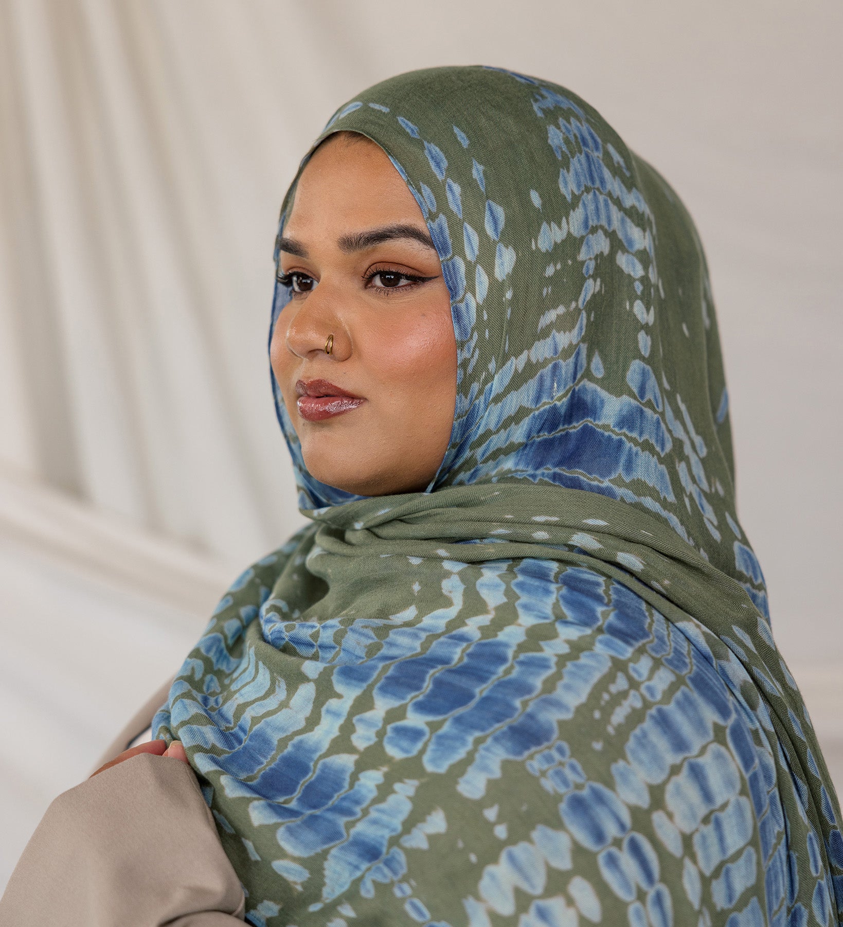 Woman wearing a green and blue Mermaid Ripple patterned hijab against a plain background