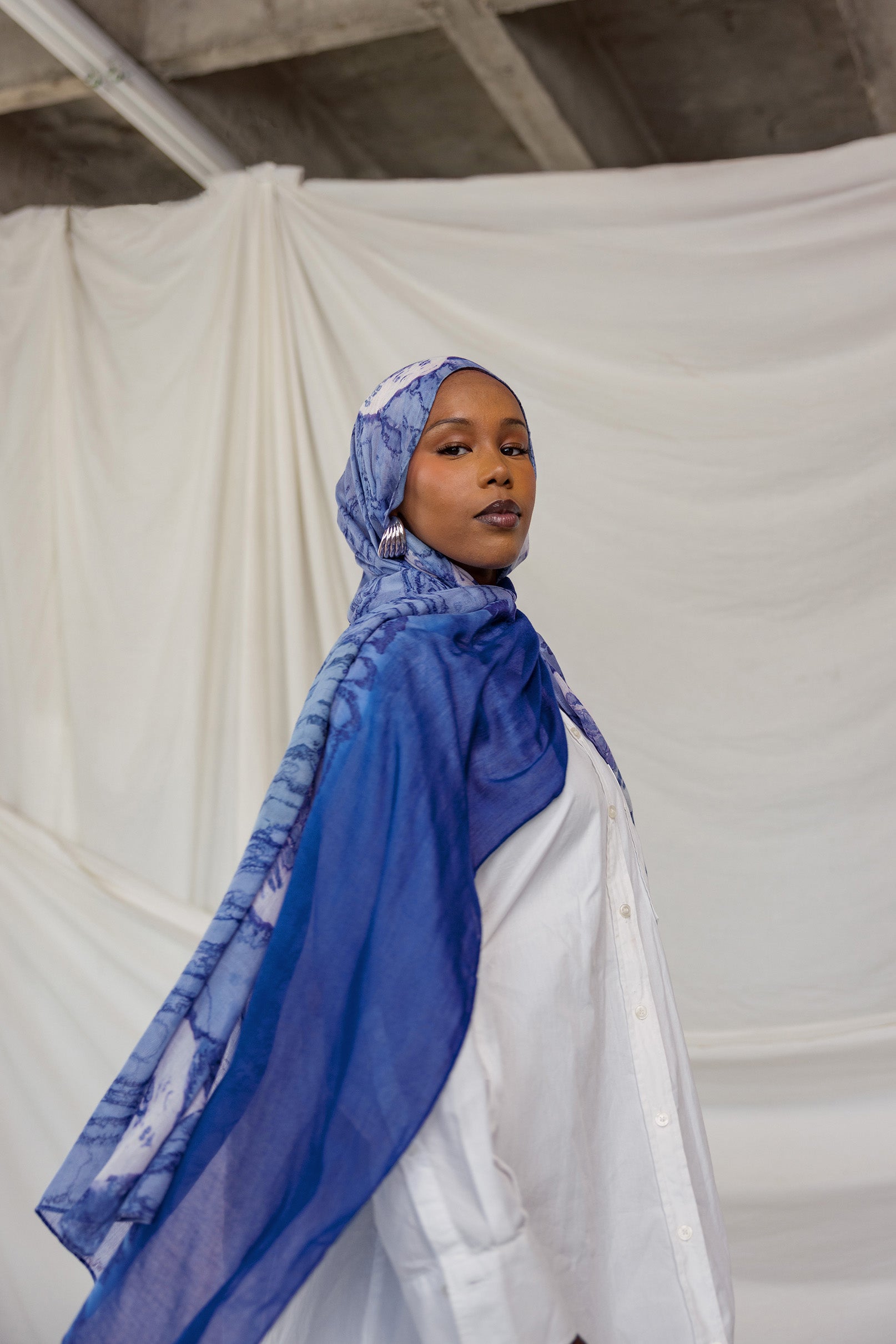 Woman wearing a royal blue and white shell printed headscarf against a plain background