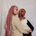 Two women wearing matching pink printed ripple pattern hijabs against a white background