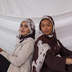 Two models shown styled in two different ways, both wearing the cream and chocolate toned print, Prairie Hide, which has splotches like a cow hide. 