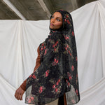 Woman wearing a black pomegranate hijab against a white curtain and concrete wall background