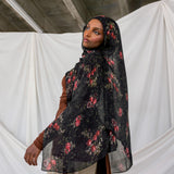 Woman wearing a black pomegranate hijab against a white curtain and concrete wall background