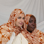 Two women wearing orange and white Amber Shells patterned hijabs against a plain background