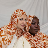 Two women wearing orange and white Amber Shells patterned hijabs against a plain background