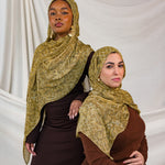 Models shown posing in the Golden Cobra scarf by VELA. This image features one model standing and one sitting, both wearing the golden/yellow toned snakeskin print. 
