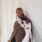 Model shown posing in Prairie Hide, a cream scarf with chocolate brown splotches. 
