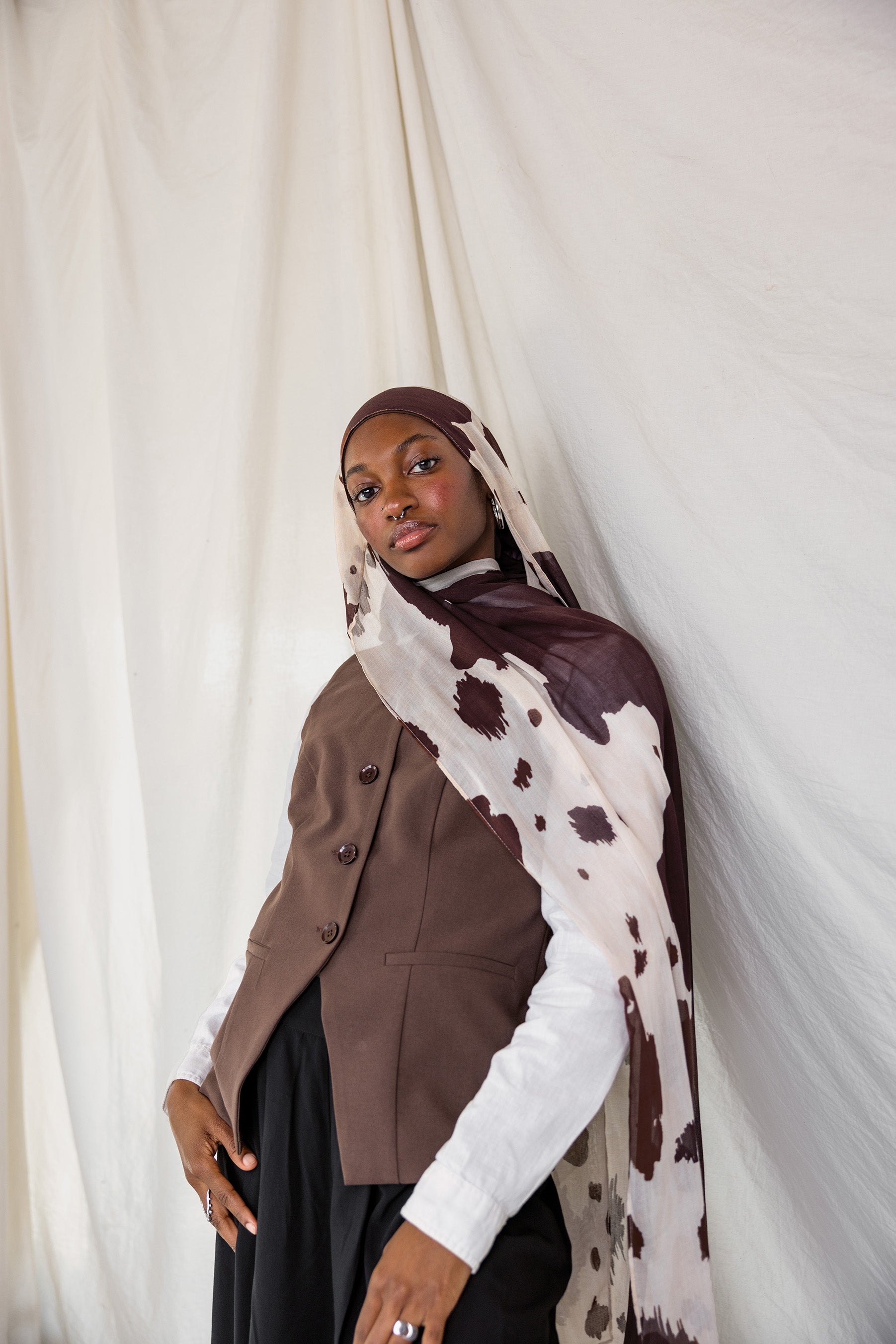 Model shown posing in Prairie Hide, a cream scarf with chocolate brown splotches. 
