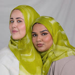 Two women wearing lime green sediment printed headscarves against a plain background