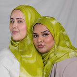 Two women wearing lime green sediment printed headscarves against a plain background