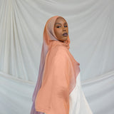 Woman wearing a bright pink / purple pastel hijab in front of draped fabric