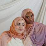 Two women wearing pink and purple ombre hijabs against a white curtain background