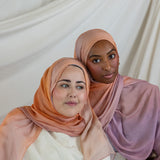 Two women wearing pink and purple ombre hijabs against a white curtain background