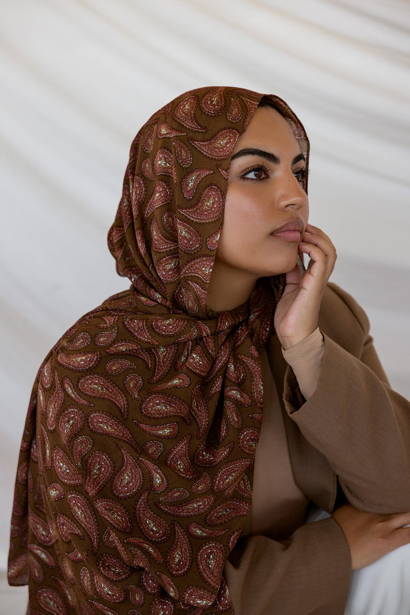 A woman wearing a brown red toned paisley print hijab. 