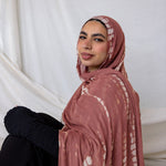Woman wearing a pink hijab with white ripple patterns against a white curtain background