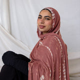Woman wearing a pink hijab with white ripple patterns against a white curtain background