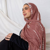 Woman wearing a patterned ripple pink printed hijab sitting against a white curtain.