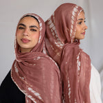 Two women wearing matching pink hijabs with a subtle white ripple pattern against a plain background