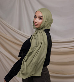 A person wearing a light olive colored hijab draped over the head, standing against a neutral backdrop.