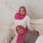 Two models shown posed in Rose Wave, a wearable version of a hot pink toned scarf. 