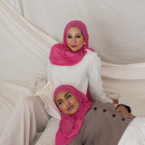 Two models shown posed in Rose Wave, a wearable version of a hot pink toned scarf. 