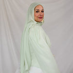 Woman wearing a light pastel green hijab against a plain background