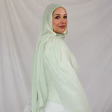 Woman wearing a light pastel green hijab against a plain background