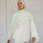 Model styled in a light pastel green hijab and white outfit against a plain background
