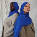 Two models shown posing together wearing Spirulina Blue, a vivid electric blue toned scarf by VELA. 
