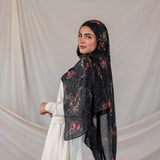 Woman wearing a dark pomegranate print hijab against a plain background