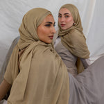 Two models shown wearing the Sandalwood scarf by VELA, which is a neutral, earthy sand color. 