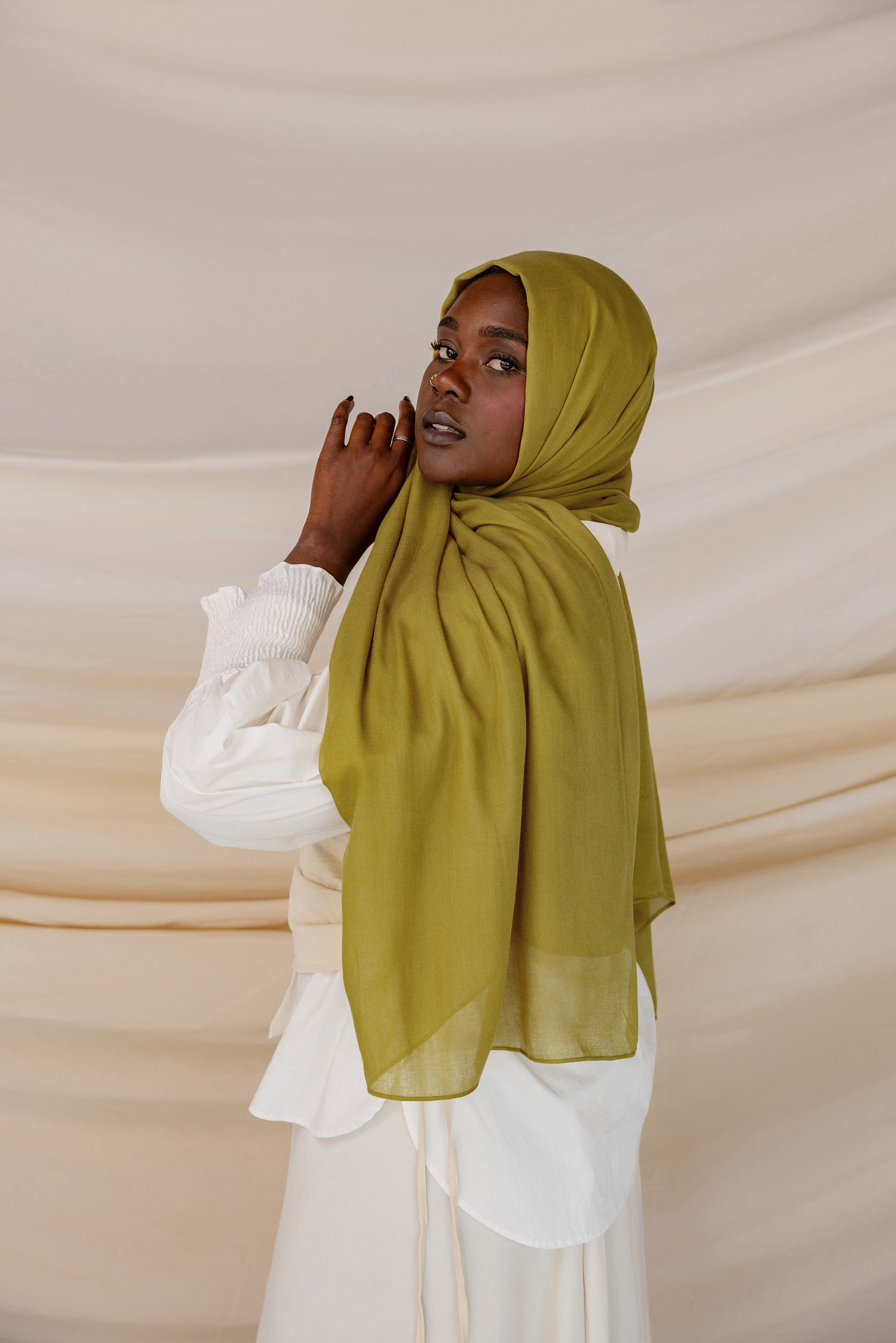 A person wearing a guava green colored hijab with a white outfit.